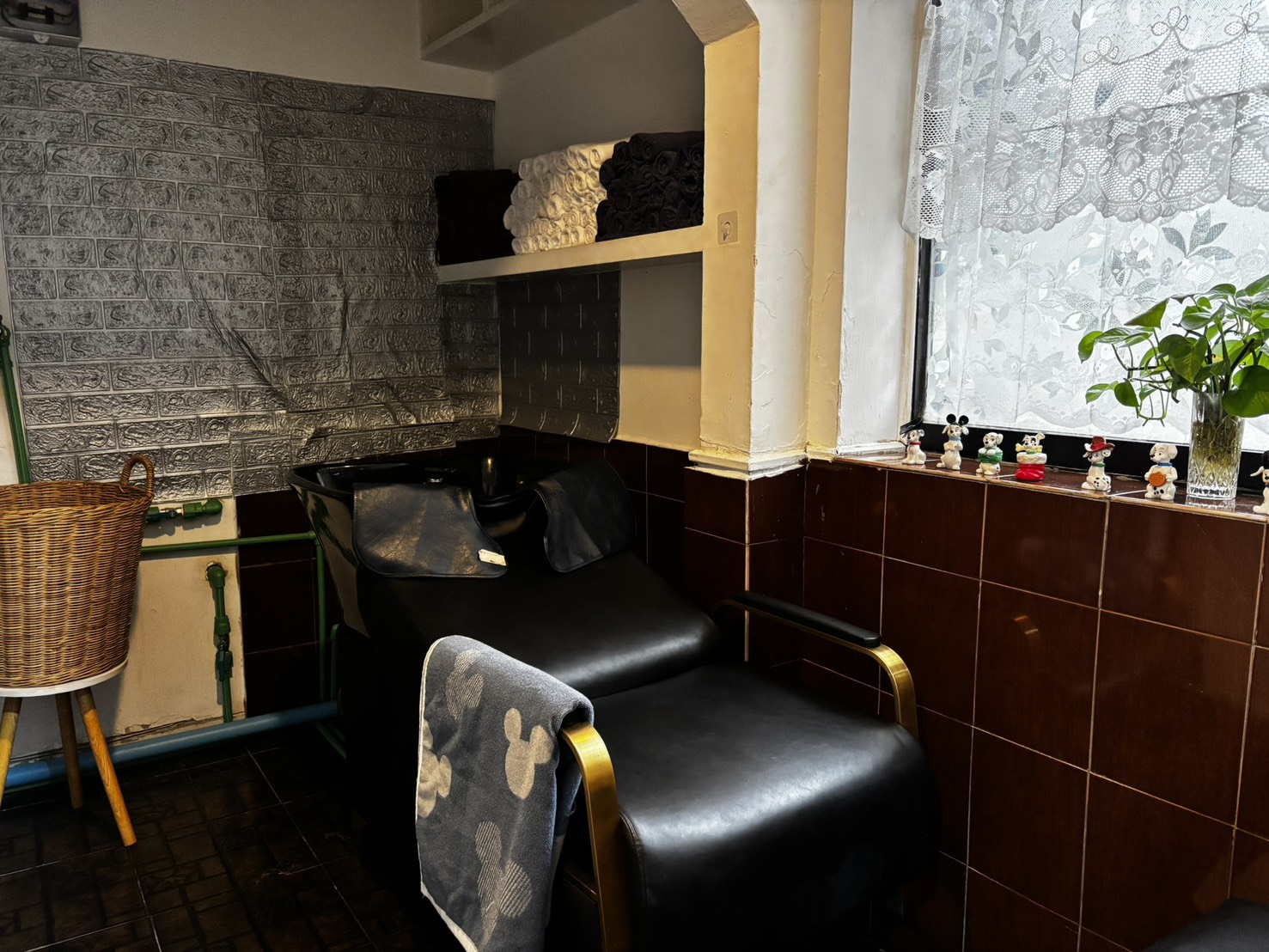 The shampoo basin beneath a lace-curtained window, rolled towels on the shelf above