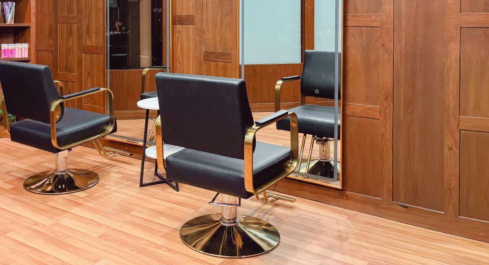Black leather styling chairs with brass arms and bases on a light wood floor, before walnut panelling and arched mirrors.
