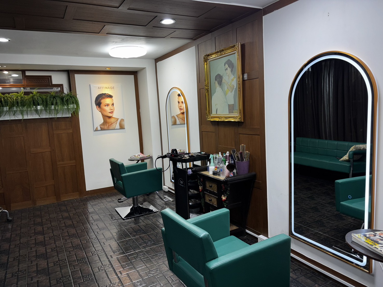 Two deep teal chairs facing lit arch mirrors, dark wood panelling, ferns above the reception counter