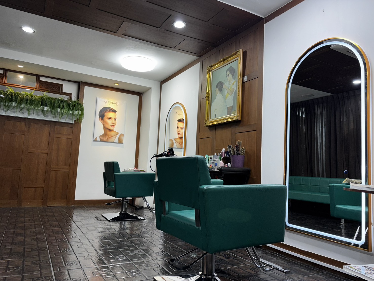 The salon interior — two deep teal chairs facing lit arch mirrors, dark wood panelling